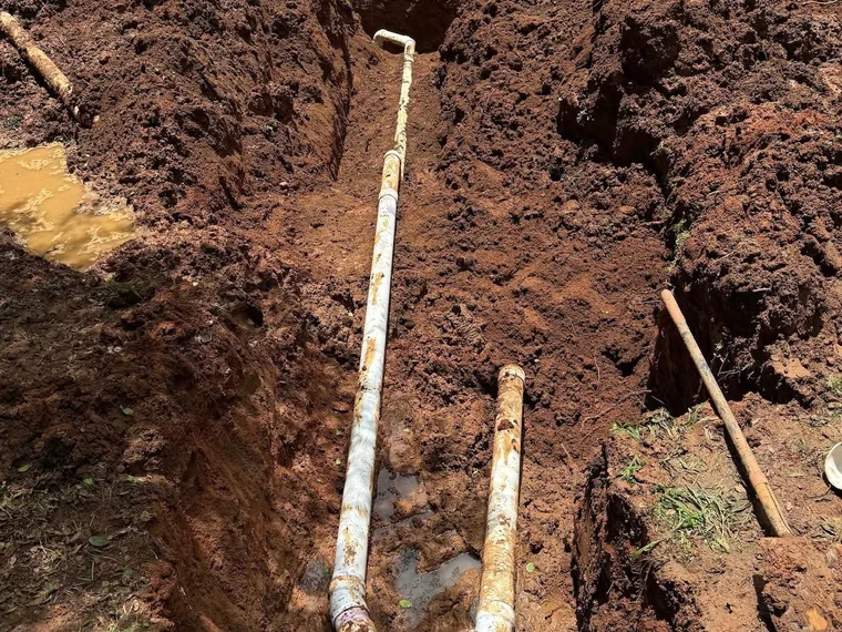 New septic drain field trench with PVC distribution piping and a wye fitting in red clay