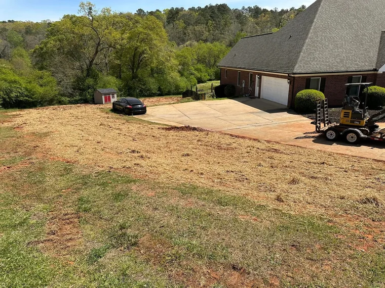 Wide view of completed drain field replacement with SepticRooter excavator on trailer and brick home in McDonough