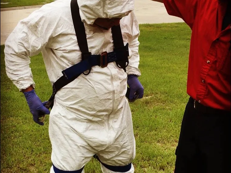 SepticRooter technician being fitted into a fall-protection harness over a Tyvek suit before confined-space entry
