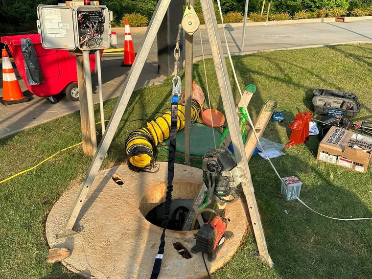 Tripod hoist with retrieval line, forced-air blower, and control panel set over an open lift station manhole